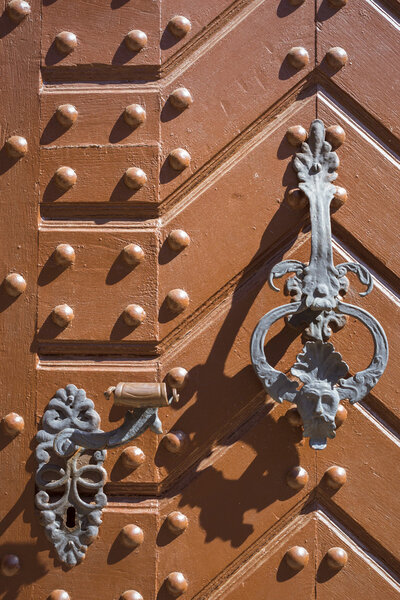 Wrought-iron bell and handle on orange door with metal rivets