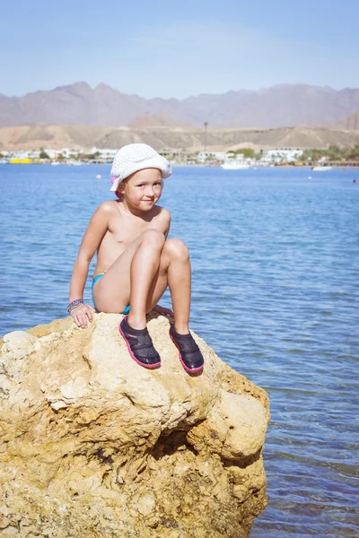 Chica en sombrero blanco sentado en una gran piedra en el centro de la playa — Foto de Stock