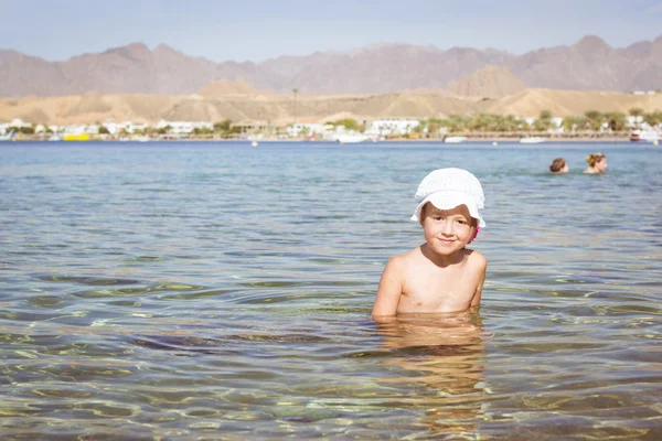 Chica en sombrero blanco sentado en un agua en medio de la playa — Foto de Stock