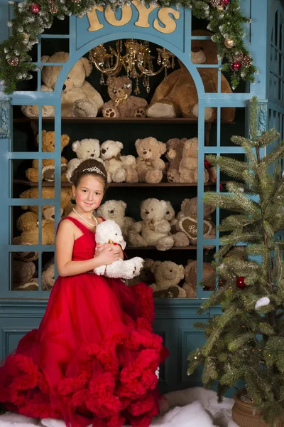 Menina em um vestido vermelho abraçando um ursinho de pelúcia — Fotografia de Stock