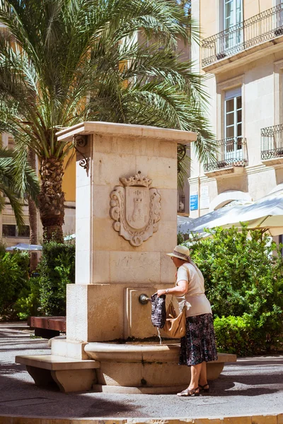 Mujer mayor recoge el agua en la fuente en el popular turista stre — Foto de Stock