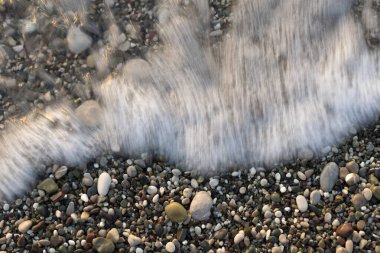 Güzel, uzun pozlu bir çekim, yumuşak, ipeksi beyaz bir deniz dalgasının çok renkli çakıl taşlarının yatağını nazikçe yıkamasını yakalar. Suyun hareket bulanıklığı, ıslak taşların keskin detaylarına karşı ruhani bir etki yaratıyor. Bu...