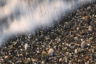 Güzel, uzun pozlu bir çekim, yumuşak, ipeksi beyaz bir deniz dalgasının çok renkli çakıl taşlarının yatağını nazikçe yıkamasını yakalar. Suyun hareket bulanıklığı, ıslak taşların keskin detaylarına karşı ruhani bir etki yaratıyor. Bu...