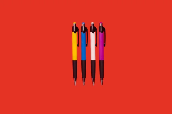 Quatre stylos colorés couchés sur un fond rouge — Photo