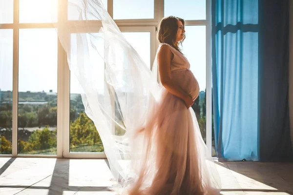 Ung söt gravid kvinna står nära fönstret — Stockfoto