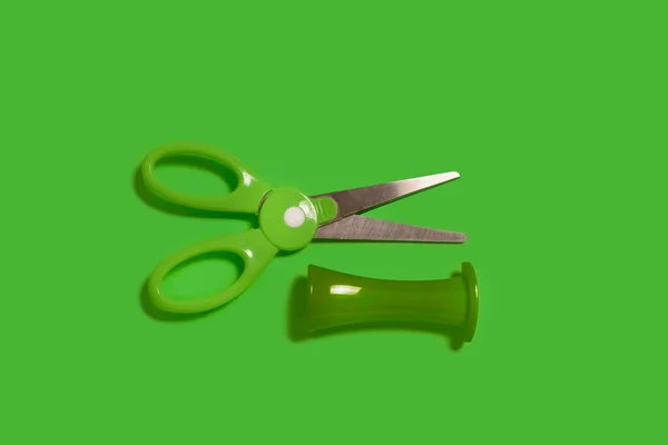 Scissors with a cap on a green background — Stock Photo, Image