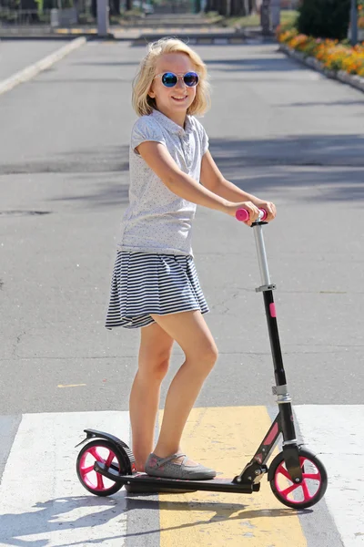 Okul çağındaki kız bir scooter sürme. Yolun bir yaya geçidi üzerinde haçlar. Telifsiz Stok Fotoğraflar