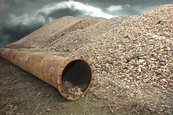 Rusty industrial  drain pipe next to a pile of gravel. — Stock Photo, Image