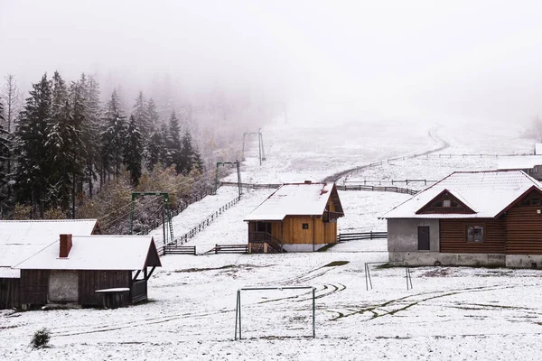 Зимовий фон з дерев'яними будинками і засніженими ялиновими деревами з туманним небом — стокове фото