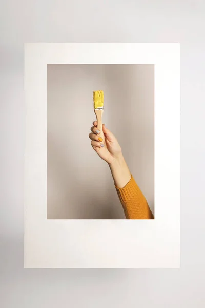 Mano con pennello e vernice gialla nel colore dell'anno 2021 in cornice surreale — Foto Stock