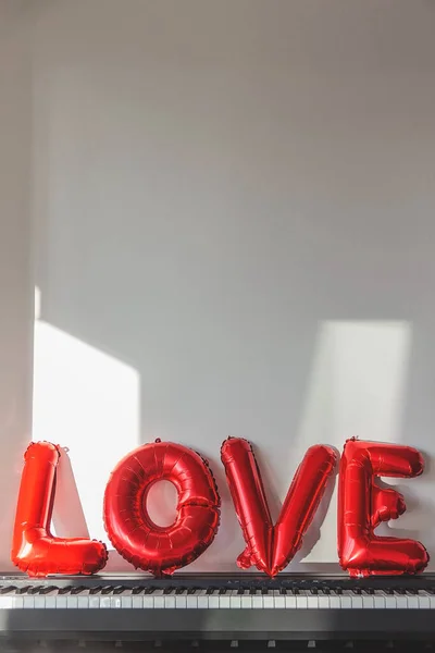 Red balloons in the shape of the word love on a home piano — Stock Photo, Image