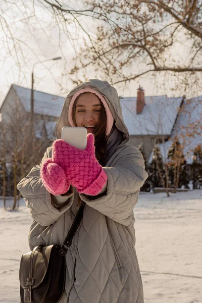 Mujer con pecas en ropa de invierno con manoplas al aire libre utiliza su teléfono inteligente —  Fotos de Stock