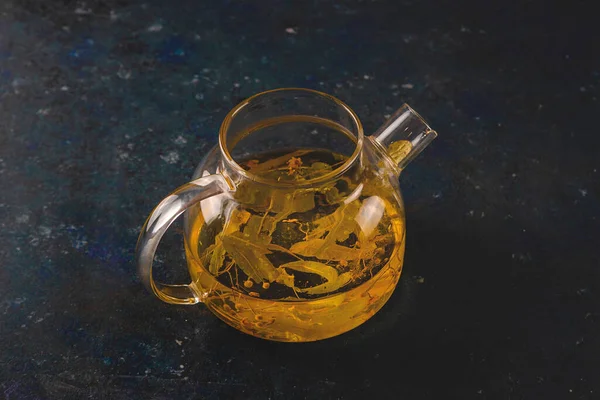 Cura de chá de ervas de tília em um bule de chá em um fundo escuro — Fotografia de Stock