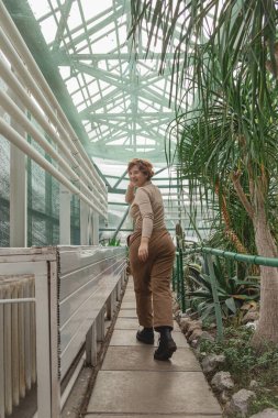 Seranın yeşil bitkilerinin arasında duran güzel, iri yarı bir kız.