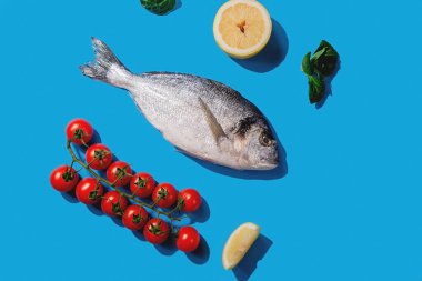 Dorado balığı, limon6 sarımsak ve parlak mavi arka planda kiraz domatesleri.