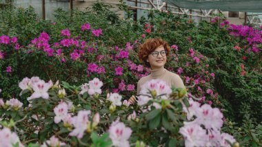 Şapkalı güzel, iri yarı bir kız seranın yeşil bitkilerinin arasında gülüyor.