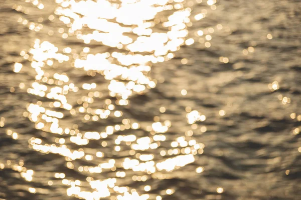 Imagem turva da textura do mar em raios de sol com pequenas ondas. Bokeh bonito da luz solar — Fotografia de Stock