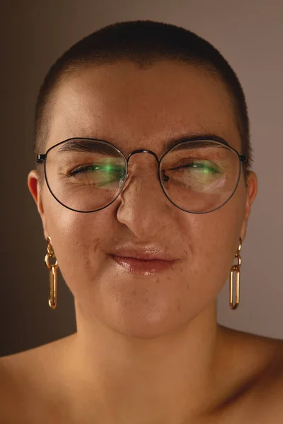 Una chica morena con el pelo corto y pecas en gafas muecas y arrugas de la nariz. —  Fotos de Stock