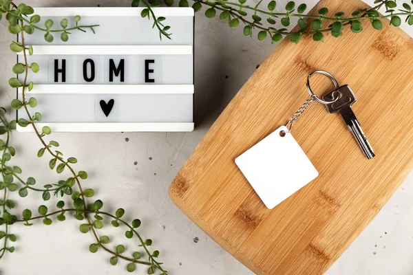Blank rhombus white sublimation keychain mockup next to board with home inscription. Key chain mockup to display design. — 스톡 사진