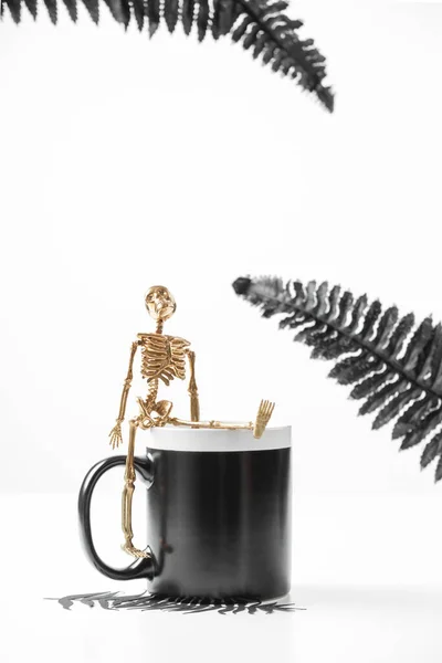 Um modelo de caneca preta. Conceito de Halloween com detalhes elegantes esqueleto dourado e folhas pretas. Fotografia de estoque estilo. — Fotografia de Stock