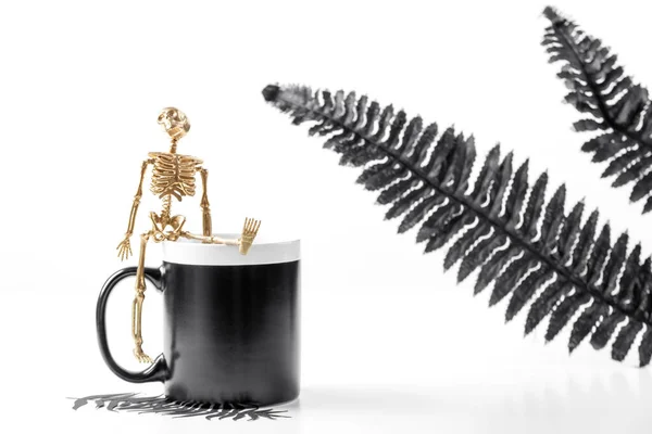 Um modelo de caneca preta. Conceito de Halloween com detalhes elegantes esqueleto dourado e folhas pretas. Fotografia de estoque estilo. — Fotografia de Stock