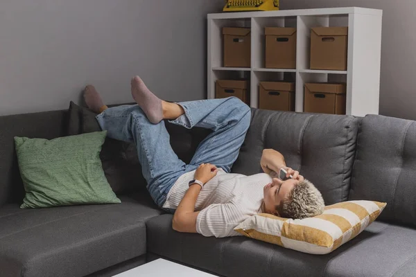 Bir kadın minimalist bir evde akıllı telefonuyla kanepede yatıyor.. — Stok fotoğraf