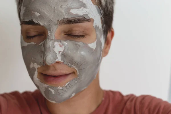 Beskuren bild av kvinna med slutna ögon tillämpa grå grön hudvård lera mask i ansiktet. Daglig skönhetsvårdsrutin. Närbild. — Stockfoto