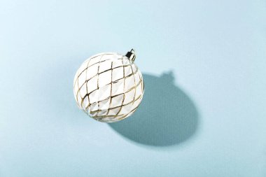 Minimalist Noel kompozisyonu. Mavi arka planda gölgeli beyaz bir Noel balosu.