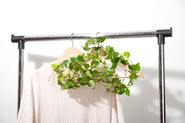 Beyaz duvarda asılı yeşil bitkilerle sarmalanmış elbise askısı. — Stok fotoğraf