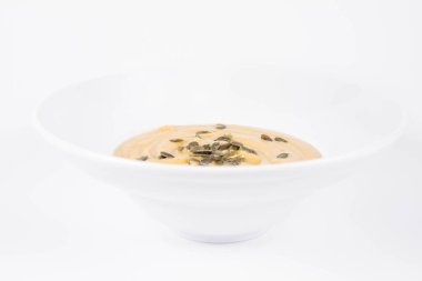 Kabak çorbası, beyaz arka planda bir tabakta kabak çekirdeği ile süslenmiş.