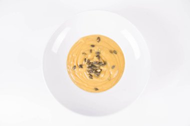 Kabak çorbası, beyaz arka planda bir tabakta kabak çekirdeği ile süslenmiş.