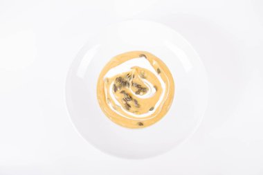 Beyaz arka planda bir tabakta krema ve kabak tohumlarıyla süslenmiş balkabağı çorbası.