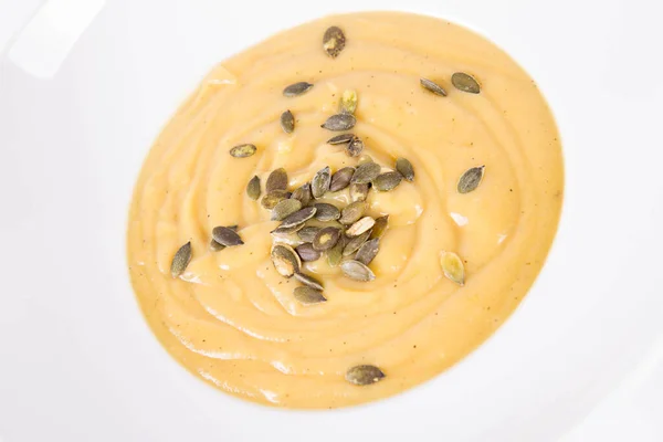 Pumpkin soup decorated with pumpkin seeds on a plate  on a white background