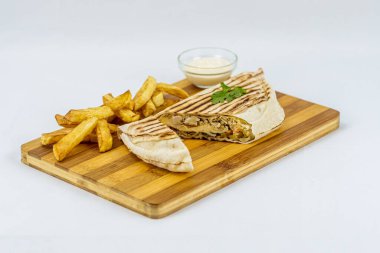 Shawarma sandwich, fresh roll in lavash with French fries. Kebab served on wooden board.