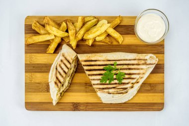 Shawarma sandwich, fresh roll in lavash with French fries. Kebab served on wooden board.