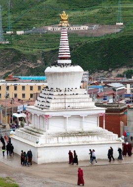 Monks and Tibetan people walking around white stupa  clipart