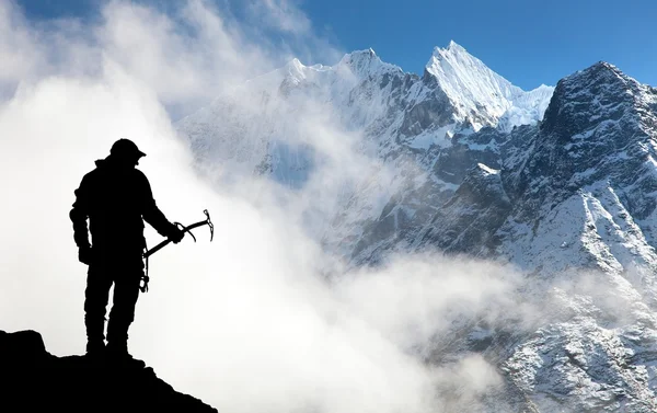 Silhouette of man with ice axe in hand and mountains — Stock Photo, Image