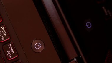 Dizüstü bilgisayarın güç düğmesi mavi yanıp sönüyor ve koyu renk bir bilgisayarın monitörüne yansıyor. İşe ara verelim. Cihazlardan uzak dur. Üst görünüm.