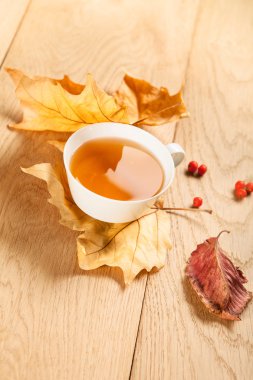 Bir fincan çay düşen sonbahar ile akçaağaç ve meyveler rowan ahşap masa arka plan üzerinde bırakır