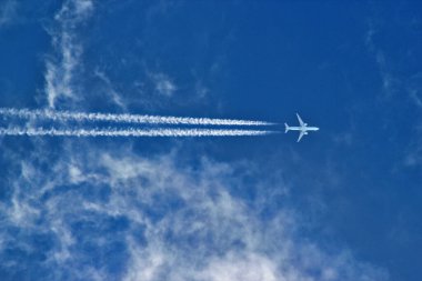 Uçan uçak beyaz çizgiler bırakır açık renkli bulutlu mavi gökyüzüne karşı
