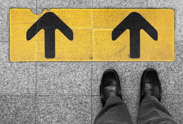 Business man standing on road with direction arrow