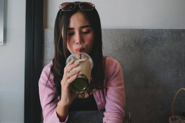 Kız elinde plastik bir bardak kibrit, peçeteyle sarılıp pipetle su içiyor.