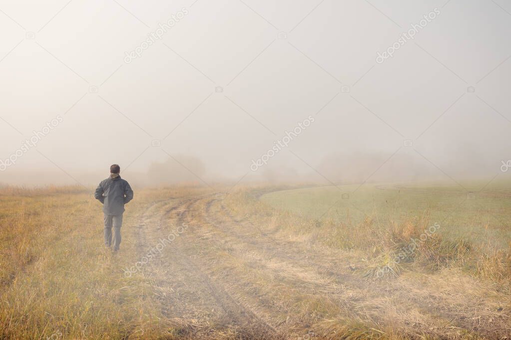A person walk into the misty foggy countryside, rural road in a dramatic mystic sunrise scene with abstract colors