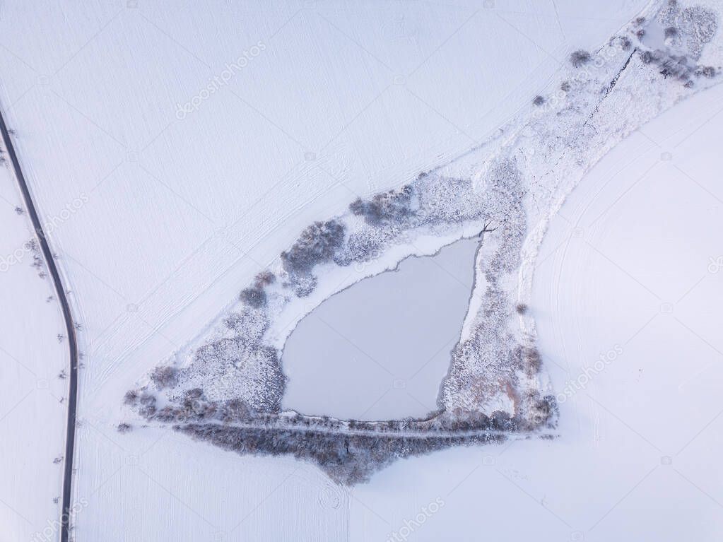 Aerial bird view of beautiful winter landscape with frozen pond covered with snow. Central european countryside. Czech Republic, Vysocina Highland region, Europe