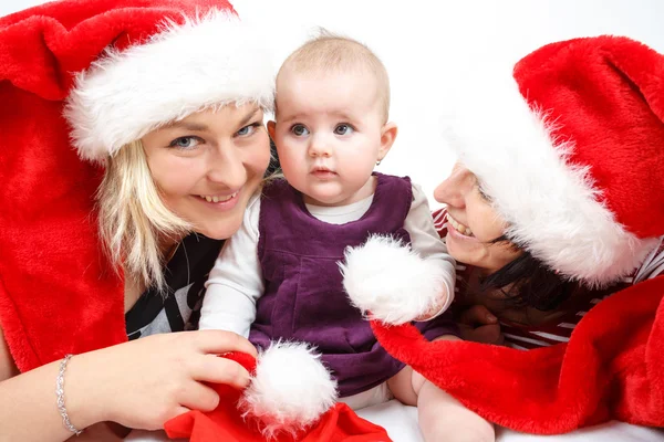 Bebé sonriente con dos mujeres con sombreros de santa —  Fotos de Stock