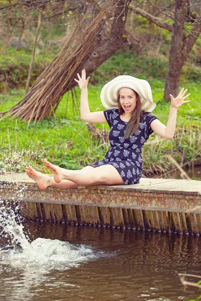 Mulher na moda alegre senta-se na pequena ponte e salpicando a água — Fotografia de Stock