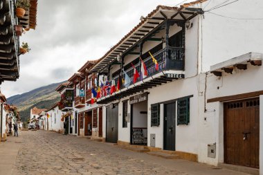 Villa de Leyva, Boyaca, Colombia - November 19 2023: View of the arcade of a historic building, with pedestrians and a motorcycle passing underneath the arches.