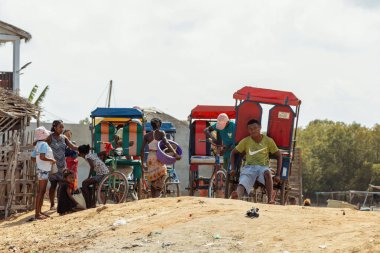 Morondava, Madagascar - November 3 2022: Local people and rickshaw drivers (pousse-pousse) gathered on a dusty street corner in the Nosy Kely area of Morondava.