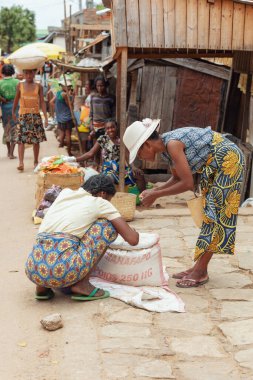 Miandrivazo, Madagascar - October 11 2025: Malagasy women in colorful lamba trading goods from a large sack on the bustling market street of Miandrivazo.