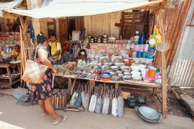 Miandrivazo, Madagascar - October 11 2025: Local woman shopping at a street stall selling kitchenware and agricultural tools in the Miandrivazo market.